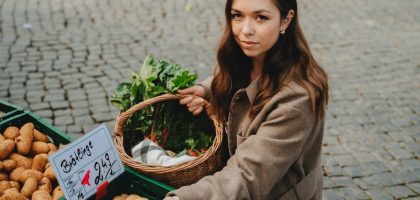 Young woman shopping at Erfurt farmers market, holding basket with fresh vegetables. Capturing local shopping culture.
